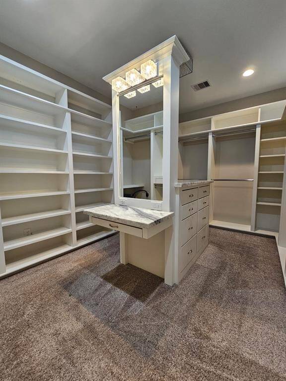 Primary bedroom closet with island and sitting vanity.  Built in shoe shelves and hanging racks.
