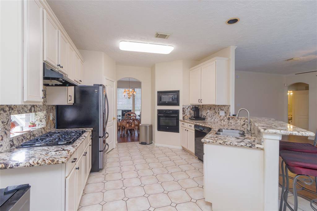 Kitchen features cabinetry, granite countertops, oven and built in microwave, and a tiled floor, with a breakfast bar and a view into the dining area.