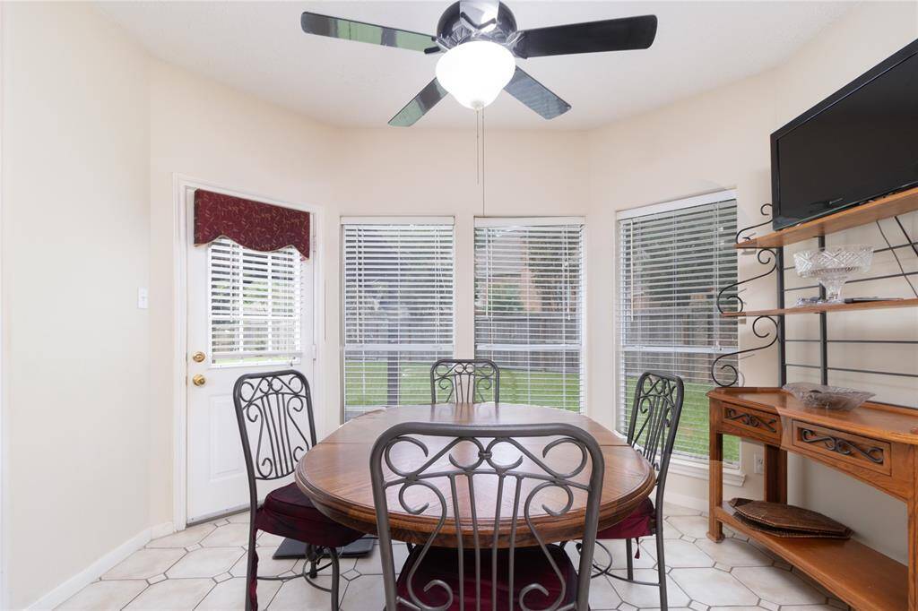 Bright, cozy breakfast nook featuring tiled floors, a ceiling fan, ample natural light from windows with blinds, and a door leading outside to covered patio.