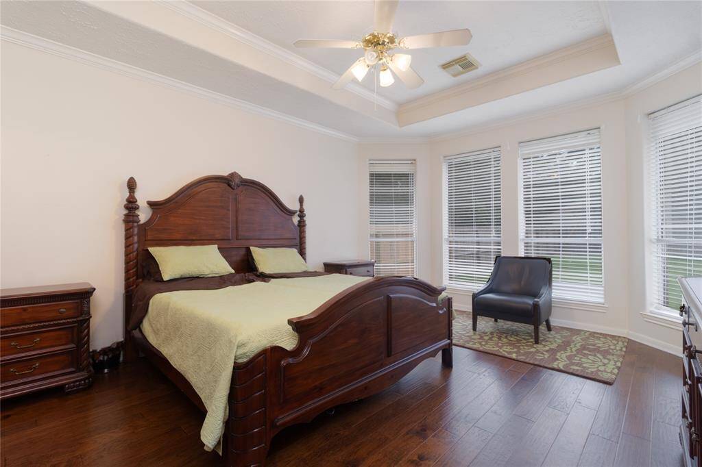 Primary bedroom has a ceiling fan, hardwood flooring, and ample natural light from large windows with blinds.
