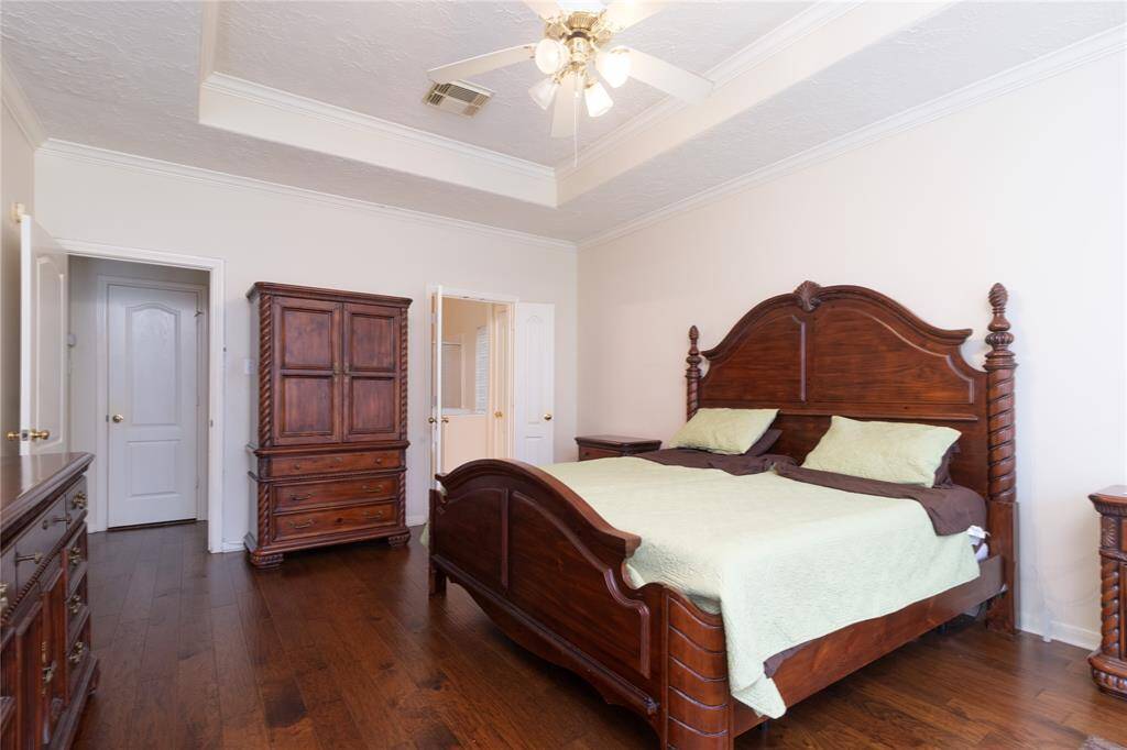 Primary bedroom featuring hardwood floors, a tray ceiling with a ceiling fan and door leading into en-suite bathroom.