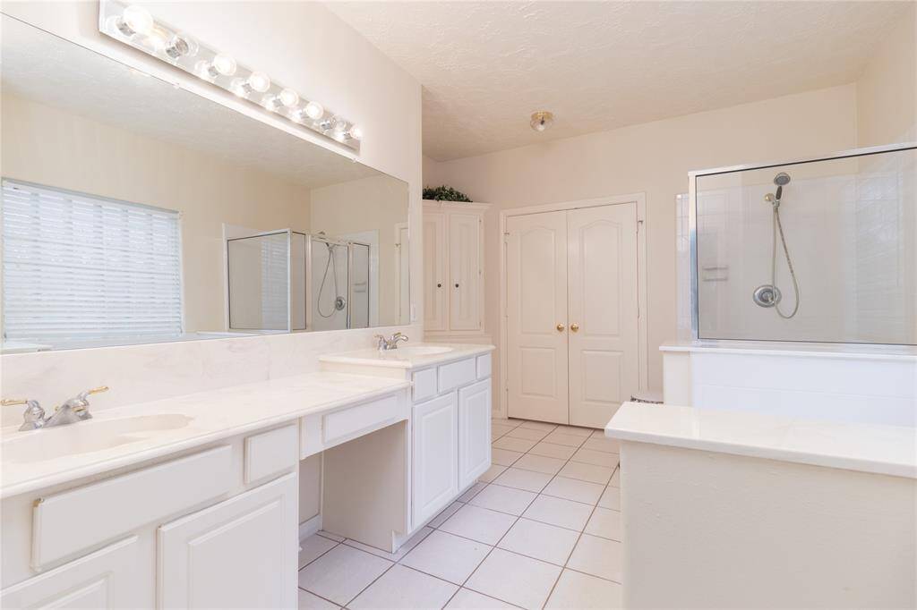 Bright, spacious bathroom featuring a large vanity with dual sinks, ample cabinetry, a private toilet area, and a walk-in shower. The space benefits from natural light through a window with blinds.