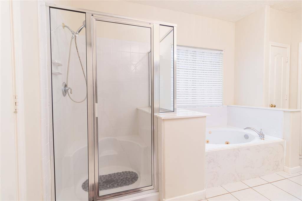 Bathroom features a separate shower with glass doors and a large corner jetted tub, offering a bright and clean space with natural light from the window.