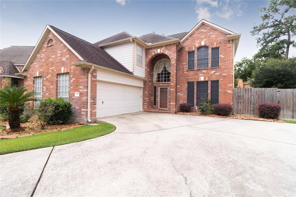 Two-story brick home featuring an arched entryway, a two-car garage, and tall windows, set in a residential neighborhood with a concrete driveway and a well-maintained lawn.
