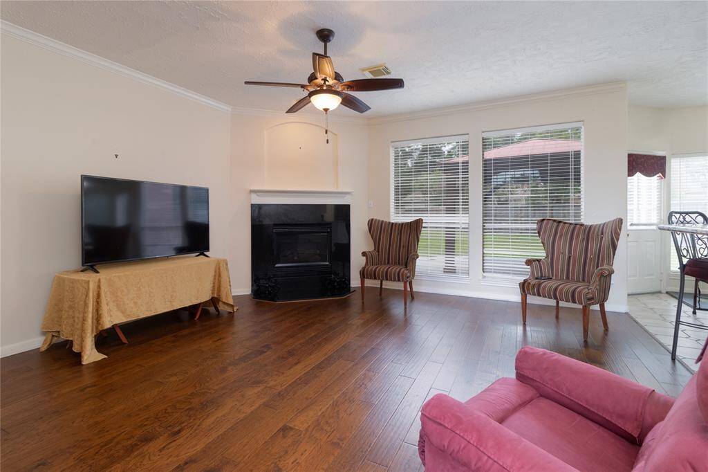 Den with hardwood floors, a cozy fireplace, ample natural light from large windows, and a ceiling fan for comfort.