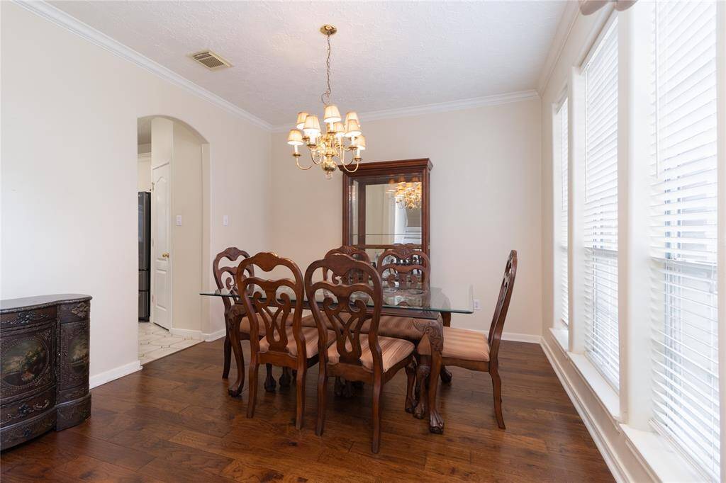 Well-lit dining room with large windows, elegant hardwood floors, and a traditional chandelier.