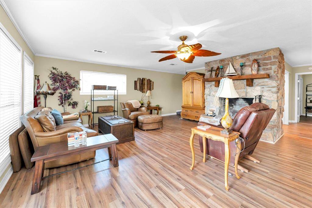 This living room features hardwood floors, a stone fireplace, and a ceiling fan, creating a cozy and inviting atmosphere.