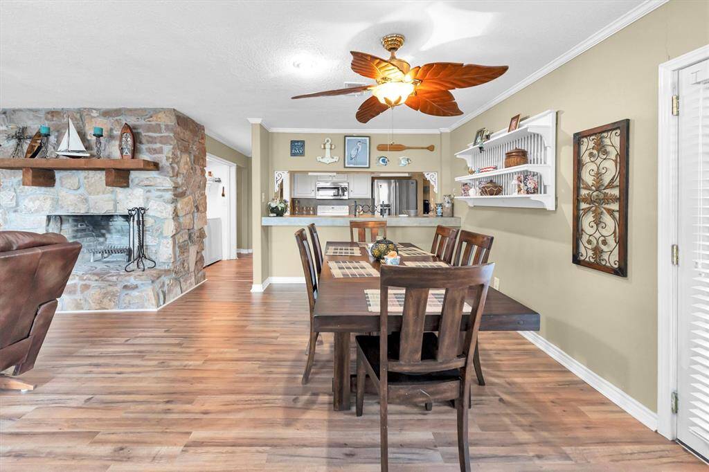 Spacious open-concept dining area with hardwood floors, leading to the kitchen. A cozy stone fireplace adds character to the room.