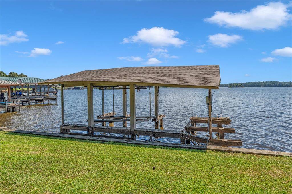 This is a waterfront property featuring a covered boat dock with a lift, set against a scenic lake backdrop. The well-maintained lawn slopes gently towards the water, offering easy access to boating and lake activities.