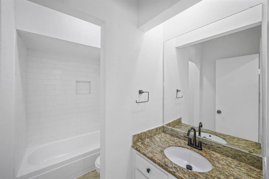 Lovely secondary bathroom complete with a granite countertops and wooden cabinets cabinets, and a shower/tub combo with a gorgeous tile shower wall.