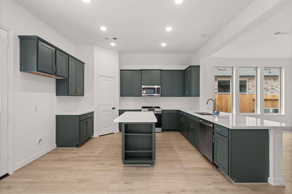This light and bright kitchen features a large quartz island, dark cabinets, a large sink overlooking your family room, recessed lighting, and beautiful backsplash.