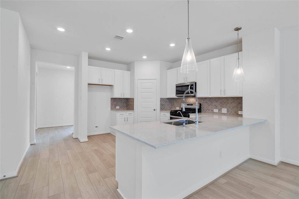 This spacious kitchen features high ceilings, stained wood cabinets, granite countertops, SS appliances, modern tile backsplash, recessed and pendant lighting, space for breakfast bar, and a pantry all overlooking your huge family room.