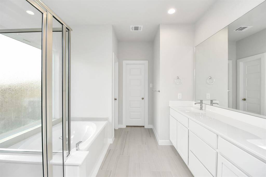Escape to a spa-like oasis in this primary bathroom. Enjoy a walk-in showerwith tile surround, a separate garden tub with custom detailing, and an elegantvanity featuring light countertops, modern hardware, and beautiful recessed lights.Experience luxury and relaxation in every detail.