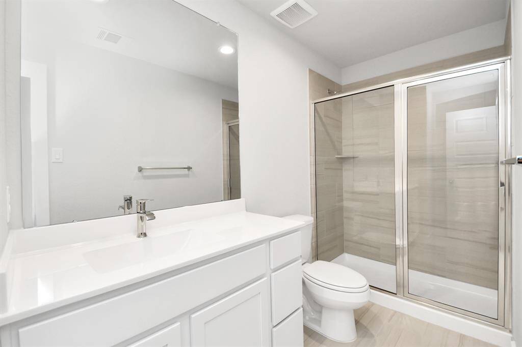 Secondary bath features tile flooring, walk-in shower with tile surround, light stainedwood cabinets, and a beautiful light countertop.