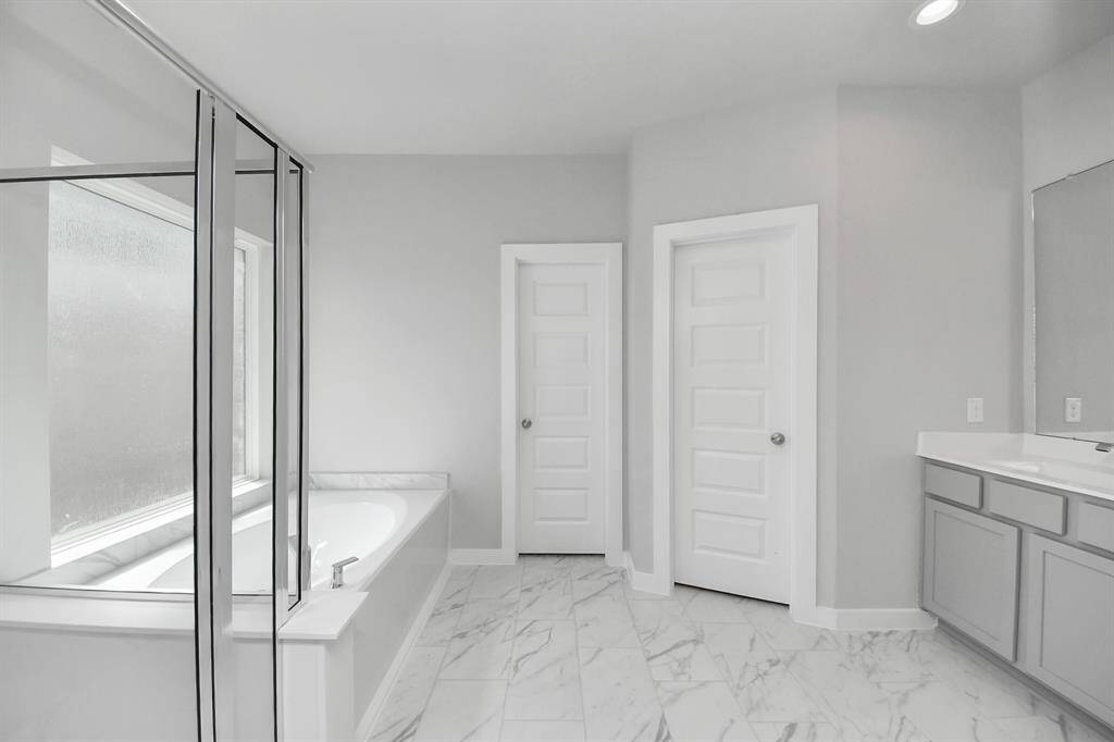 Escape to a spa-like oasis in this primary bathroom. Enjoy a walk-in shower with tile surround, a separate garden tub with custom detailing, and an elegant vanity featuring light countertops, modern hardware, and beautiful recessed lights. Experience luxury and relaxation in every detail.