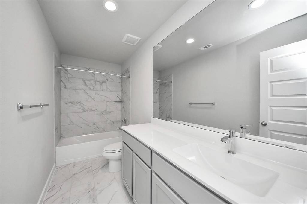 Secondary bath features tile flooring, bath/shower combo with tile surround, light stained wood cabinets, beautiful light countertop.