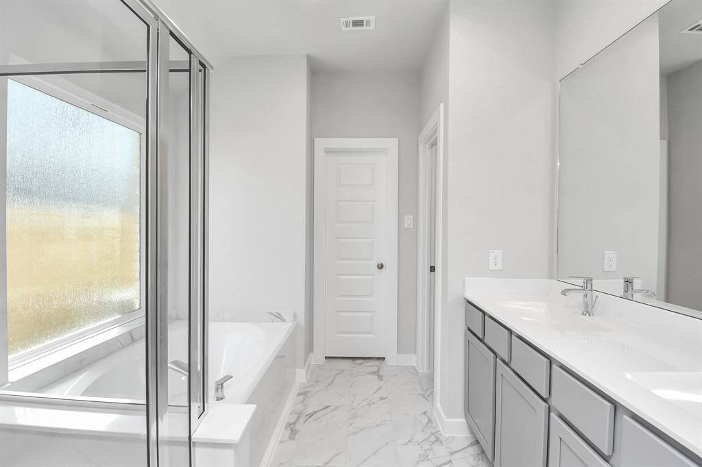 Escape to a spa-like oasis in this primary bathroom. Enjoy a walk-in showerwith tile surround, a separate garden tub with custom detailing, and an elegantvanity featuring light countertops, modern hardware, and beautiful recessed lights.Experience luxury and relaxation in every detail.