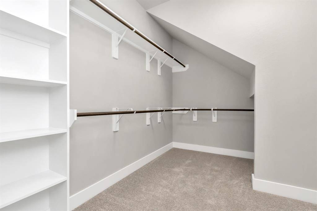 Explore the roomy walk-in closet adorned with shelving, plush carpet, custom paint, and dark modern finishes.  Sample photo, as built color and selections may vary.