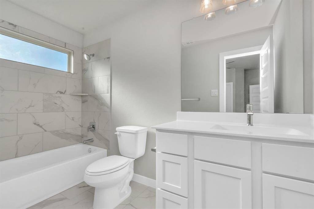 Secondary bathroom. Bath/shower combo with tile surround, light wood cabinets complete with a beautiful light countertop, this bathroom combines style and functionality for a truly inviting ambiance.  Sample photo, as built color and selections may vary.