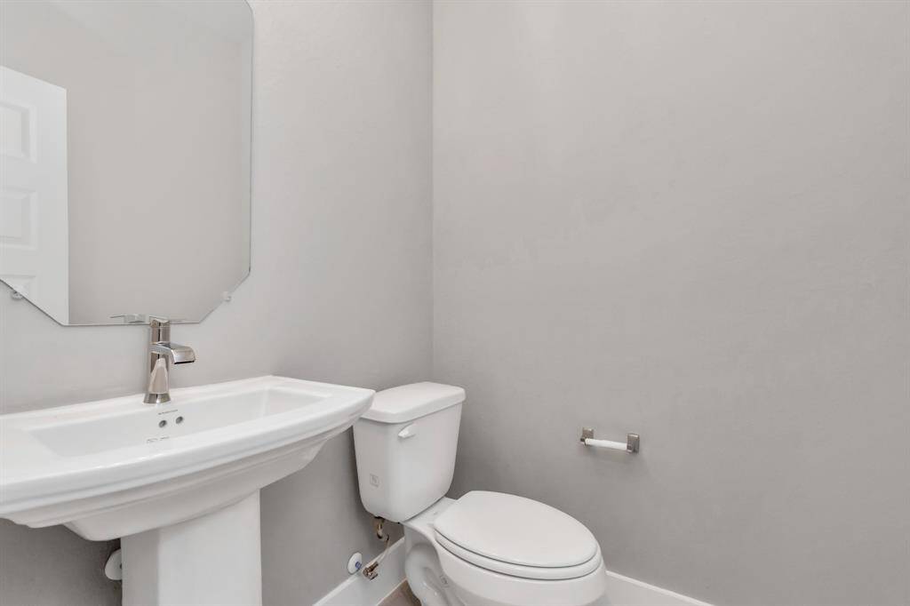 A glimpse of the spacious upgraded half bath featuring a pedestal sink, sophisticated light fixtures, and sleek hardware. Sample photo, as built color and selections may vary.