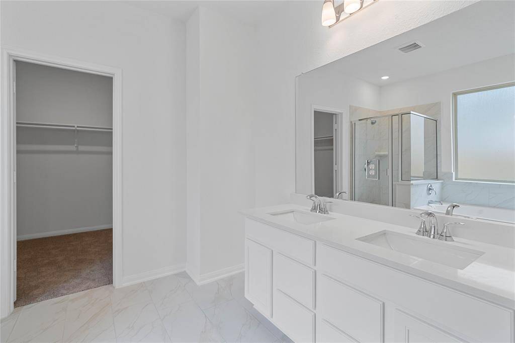 This primary bathroom is definitely move-in ready! Featuring a framed walk-in shower with tile surround, separate garden tub for soaking after a long day with custom tile detailing, light stained cabinets with light countertops, dual vanities, spacious walk-in closet with shelving, high ceilings, custom paint, sleek and modern finishes.