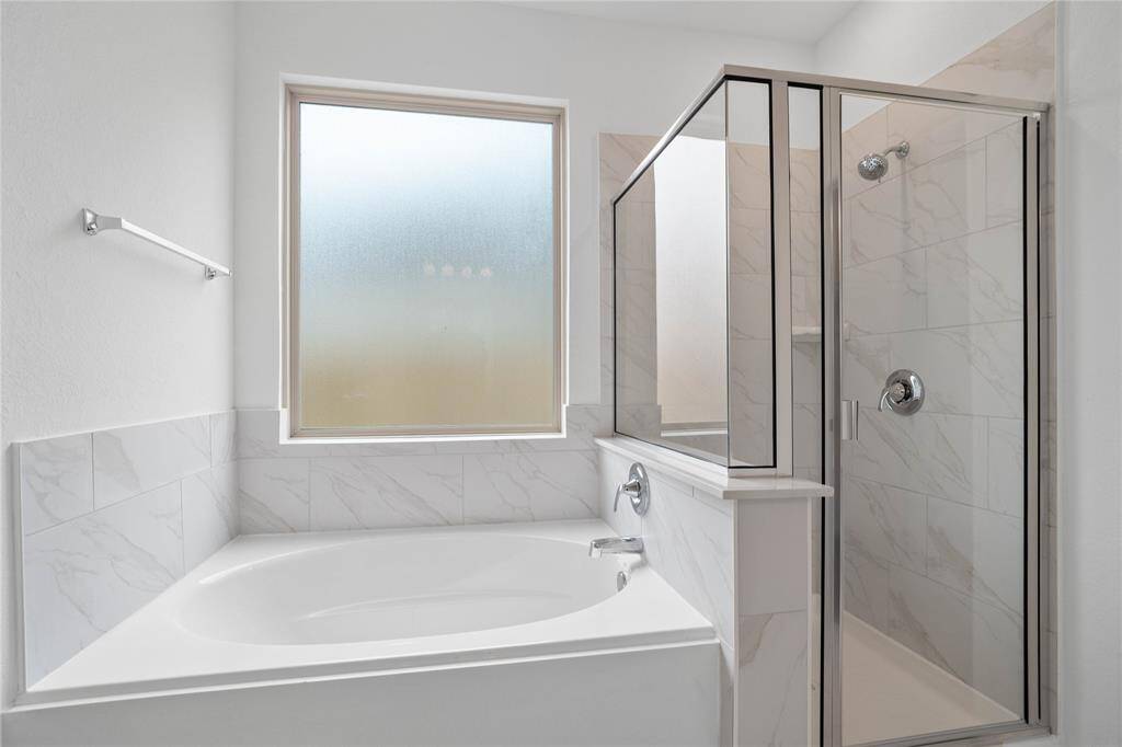 Additional view of the primary bath showcases the walk-in shower with tile surround, separate garden tub perfect for soaking after a long day, and obscure bathroom window!