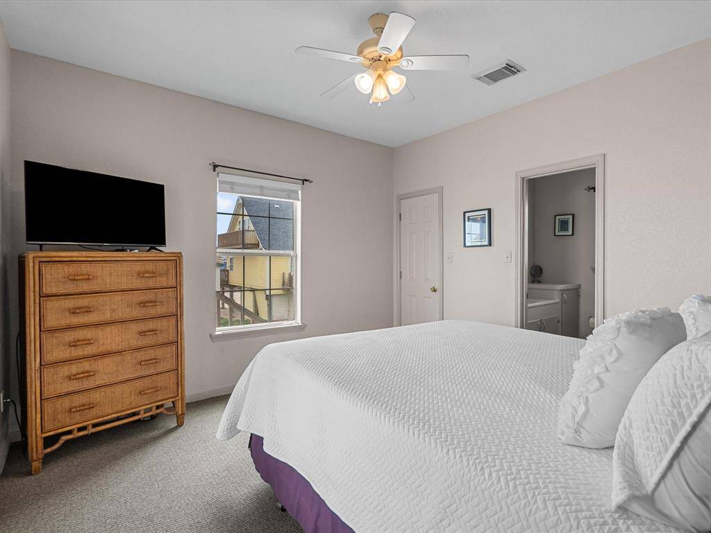 This bedroom features neutral walls, a ceiling fan, and a window with natural light. It includes a dresser with a TV and an ensuite bathroom for convenience.