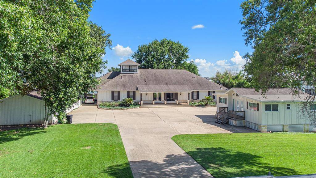 Two-story home with a large, paved driveway and an 3 car detached garage. It features a green exterior with white trim and a sizable lawn framed by mature trees. The property includes an additional single-story 3 bed/ 2 bath and full kitchen guest house. The property also features carriage house attached to the main house by a pull through breeze way.