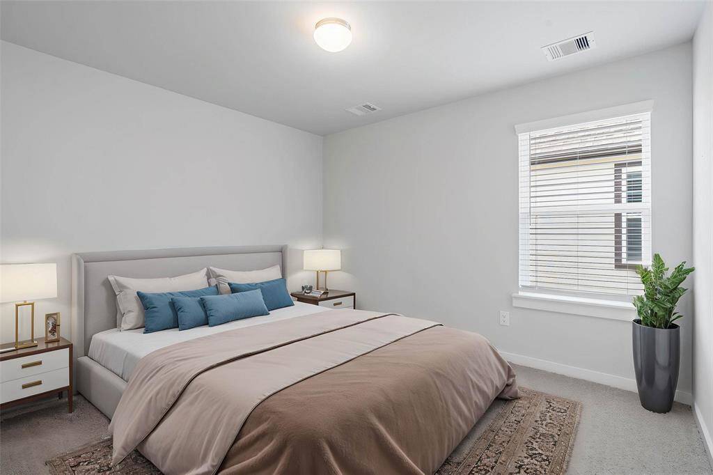 Secondary bedroom features plush carpet, custom paint, lighting, closet space, and a large window with blinds.
