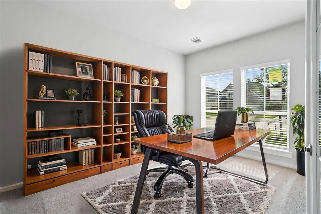 Quietly nestled in front of the home is the handsome home office. Featuring plush carpet, custom paint, large windows with blinds, and French doors!