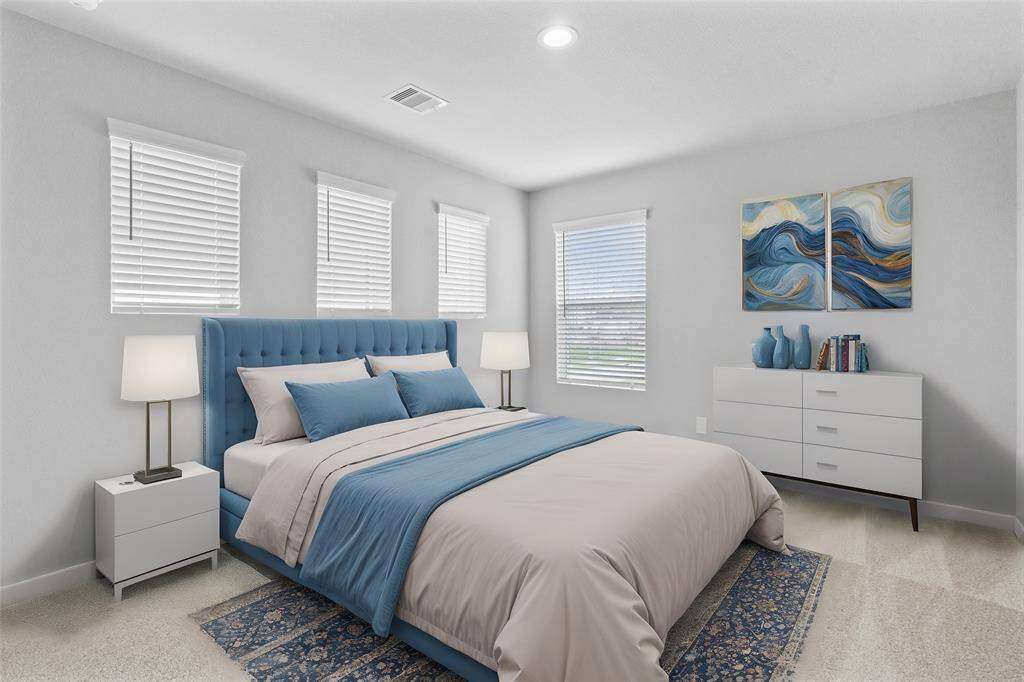 Secondary bedroom features plush carpet, custom paint, lighting, ample closet space, and large windows with privacy blinds.