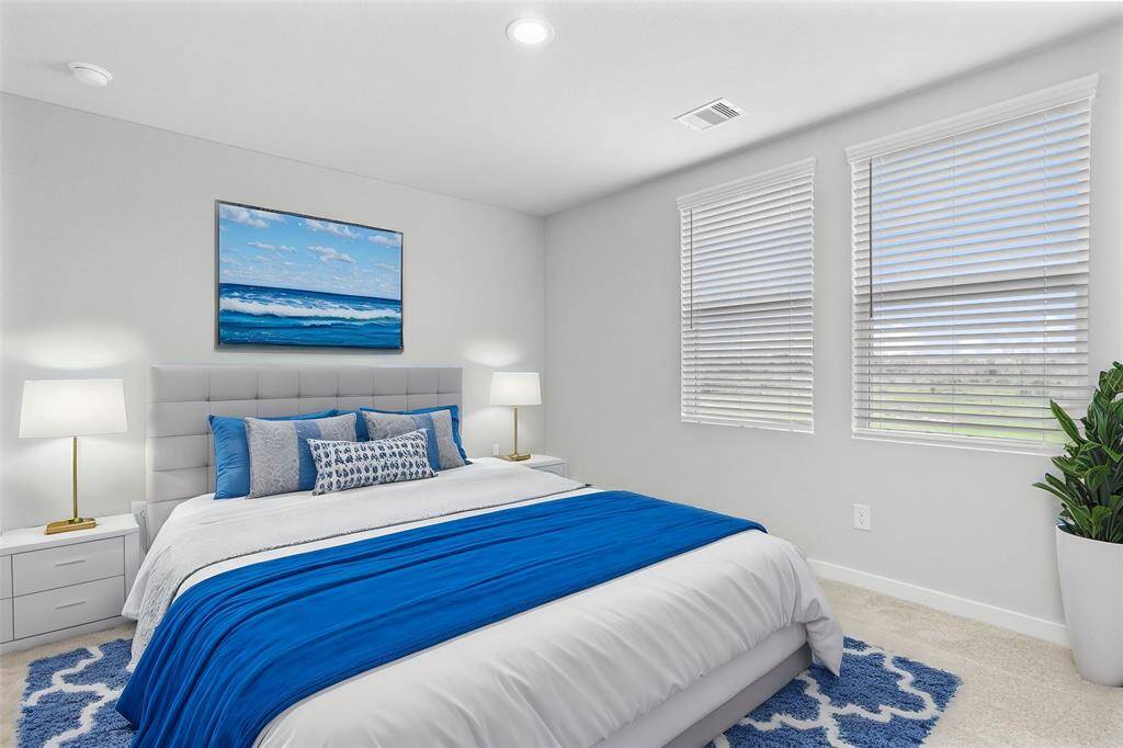 Secondary bedroom features plush carpet, custom paint, lighting, ample closet space, and large windows with privacy blinds.