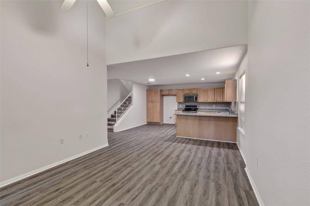 This photo shows a spacious open-plan living area with high ceilings, vinyl plank flooring, and a kitchen with ample cabinetry. There's a staircase leading to the upper level. The space is well-lit with natural light from the windows.