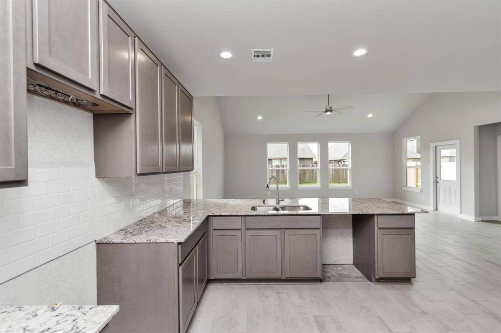 Culinary haven, featuring granite countertops, a tile backsplash, stainless steel appliances, 42” upper cabinets, and undercabinet lighting. Sample photo of completed home with similar floor plan. As-built interior colors and selections may vary.