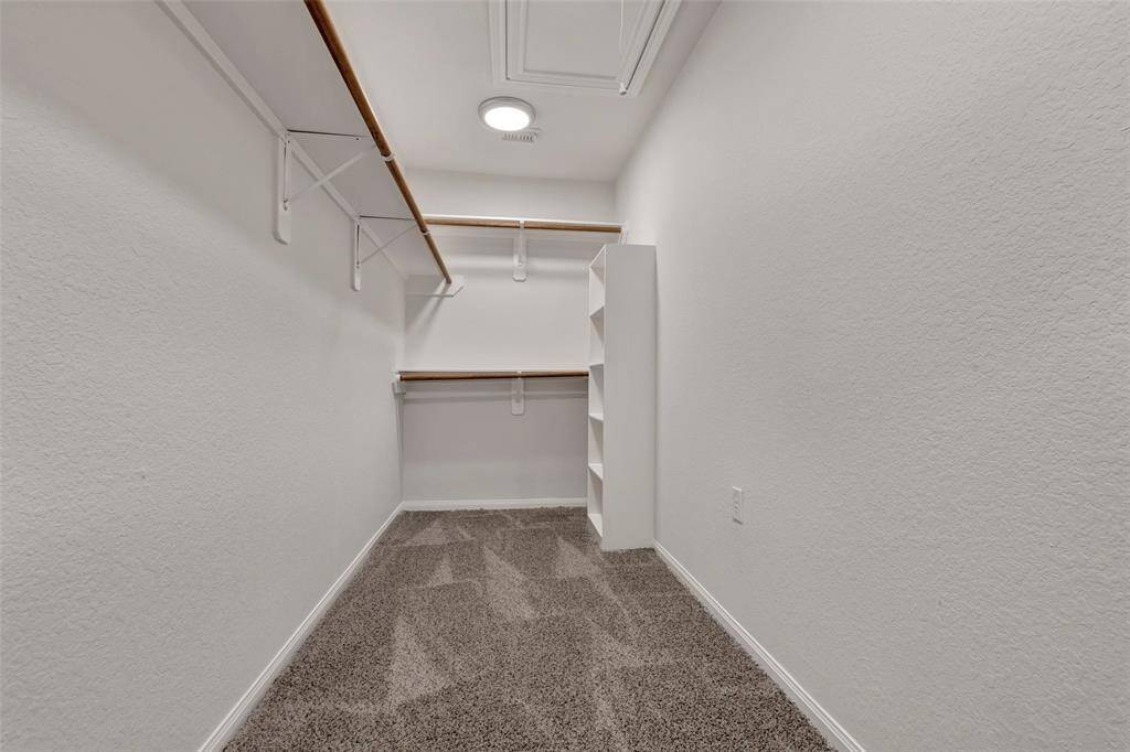 This is a spacious walk-in closet featuring ample shelving and hanging space, with a plush carpeted floor and well-lit ceiling, ideal for clothing and storage organization.