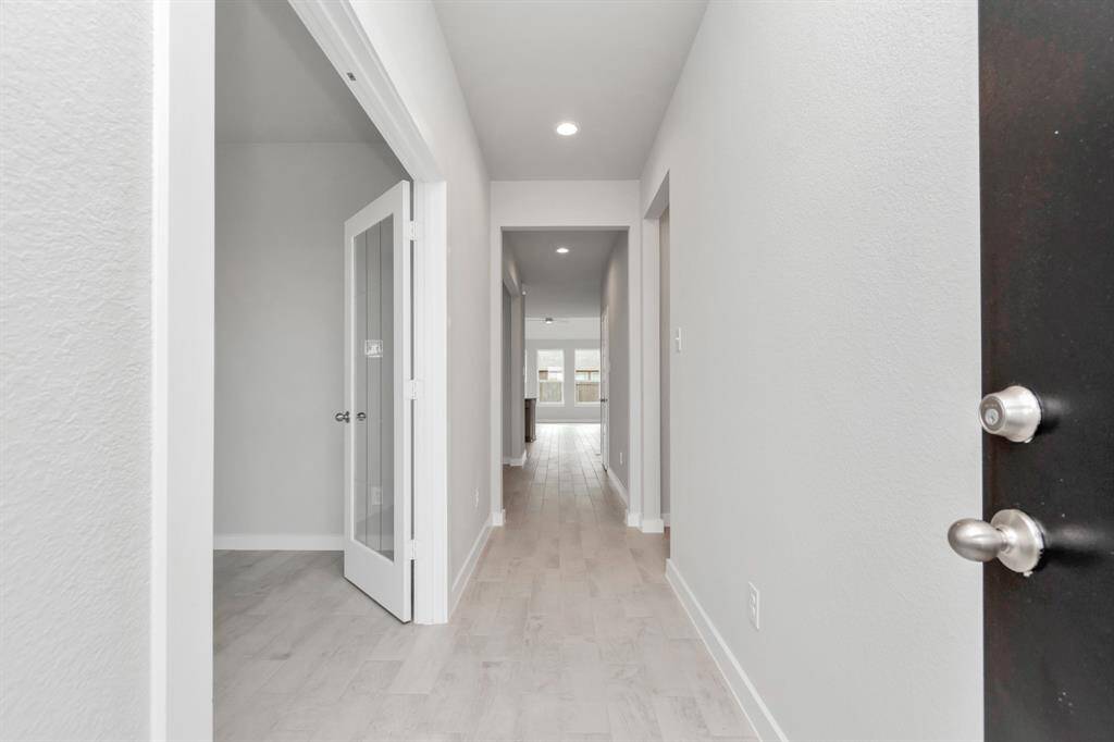 The grand entrance beckons with high ceilings, adorned with elegant wood-look tile flooring and oversized baseboards, and recessed lighting. Follow path of natural light from expansive windows ahead. Sample photo of completed home with similar floor plan. As-built interior colors and selections may vary.