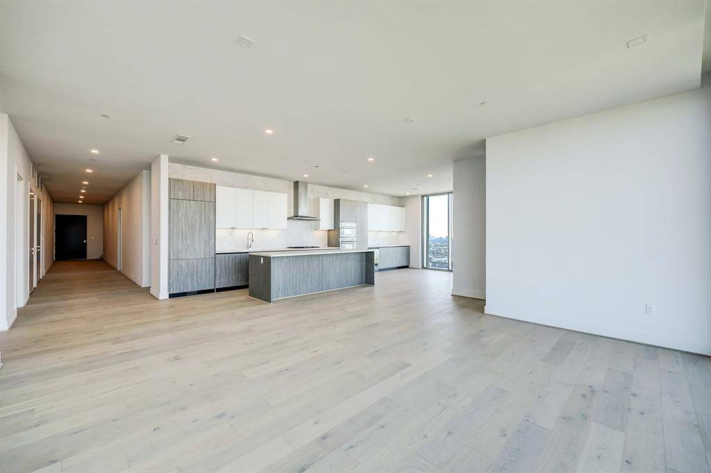 This is a contemporary, high-rise apartment featuring an open-plan living space with light hardwood floors, a sleek kitchen with a large island, Pedini Italian cabinets, porcelain counter tops and back splash and floor-to-ceiling windows offering expansive city views.