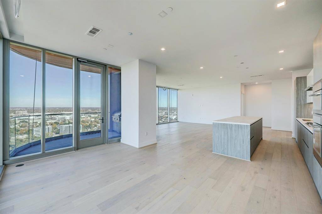Living and dining room with large floor-to-ceiling windows offering expansive city views, complemented by light hardwood floors and a clean, white interior.
