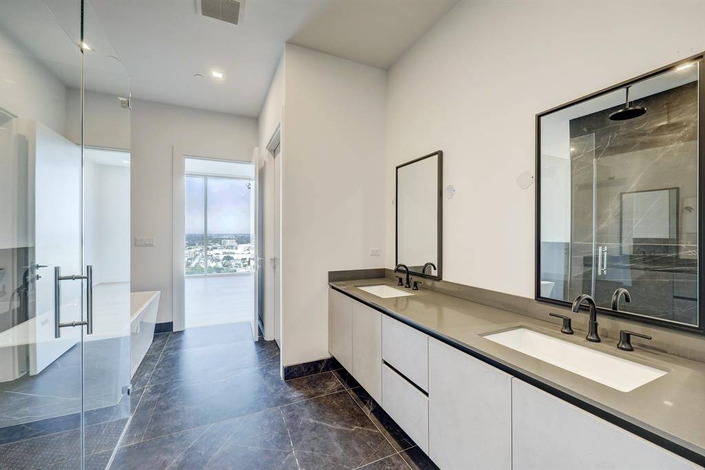 The primary bathroom features a double vanity with sleek a countertop, dark fixtures, and large mirrors. Additional features include a  large soaking tub and separate edgeless stand up shower.