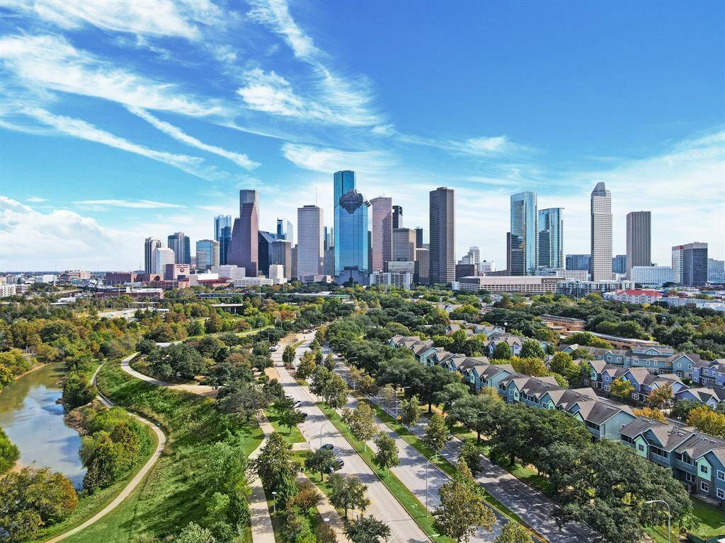 Modern design and glass windows exude sophistication, while a warm glow from the setting sun highlights its elegance. Private balconies with lush greenery offer panoramic views of downtown Houston.