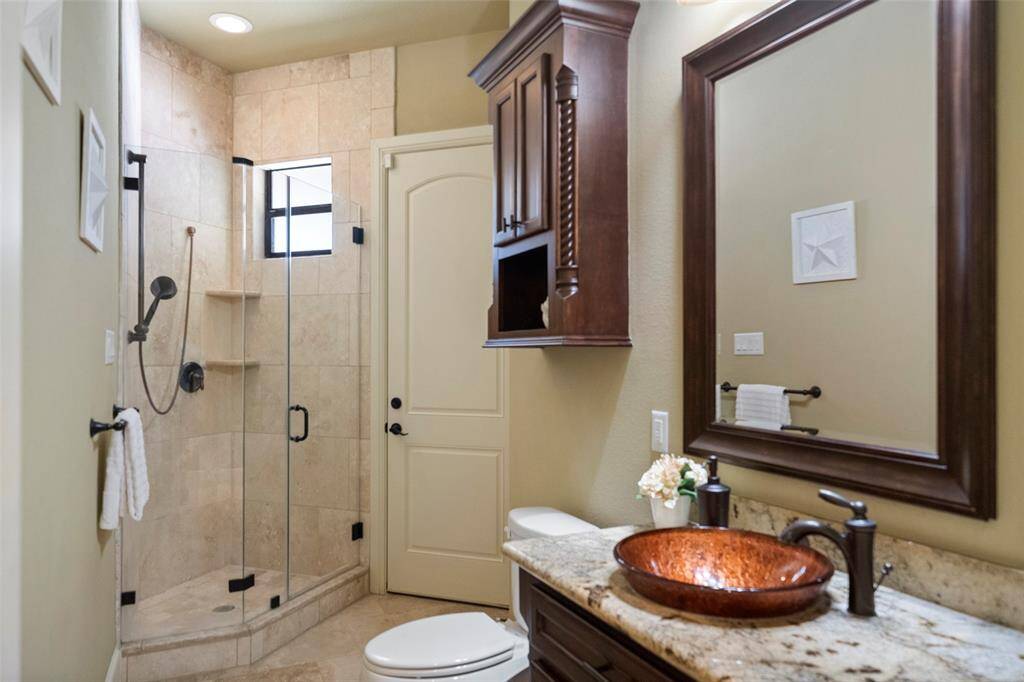 Elegant Poolside Guest Bath: This sophisticated bathroom boasts a sleek walk-in shower, a stylish vessel sink atop custom cabinetry, and a convenient direct access to the pool and spa area—perfect for refreshing after a swim.
