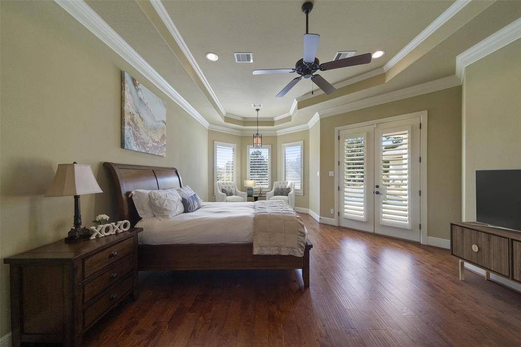 Spacious master suite featuring elegant hardwood floors, a coffered ceiling with ceiling fan, and a cozy sitting area.