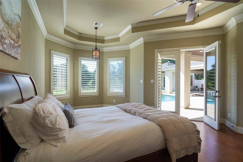 Discover tranquility in this sophisticated primary suite with stylish plantation shutters and inviting French doors leading to a serene pool and spa retreat.