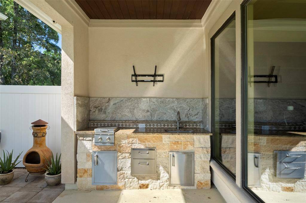 Entertain in style with this sleek outdoor kitchen, complete with a premium built-in grill and ample storage, all framed by a beautiful natural view through expansive glass doors.