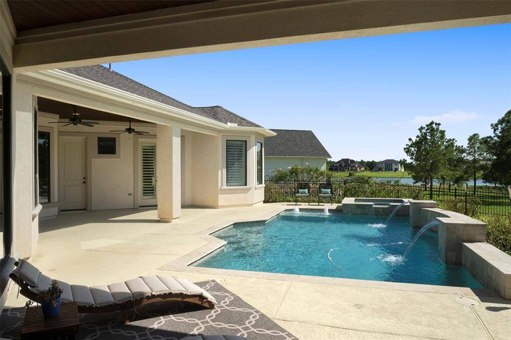 This home features a covered patio with ceiling fans, an inviting in-ground pool with water features, and a serene lake view, perfect for outdoor relaxation and entertainment.