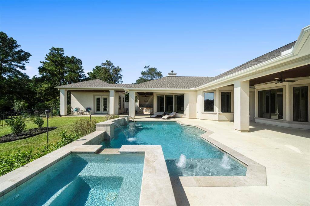 This is a spacious backyard featuring an elegant in-ground pool with an attached hot tub, complemented by a large patio area and a well-maintained lawn. The single-story home has a modern design with large windows and a covered outdoor seating area, perfect for relaxation and entertainment.
