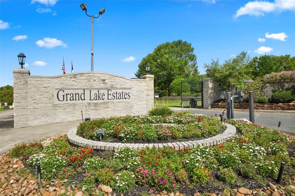 This photo shows the landscaped entrance to Grand Lake Estates, featuring a stone sign with the community name, a circular flower bed, and a gated entry, suggesting a well-maintained and secure neighborhood.