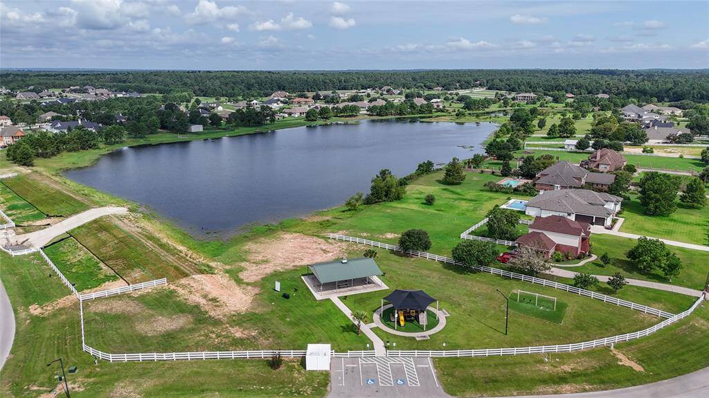 This aerial photo showcases a serene suburban community with spacious properties bordering a large, tranquil lake. A well-maintained park with a gazebo and playground adds to the neighborhood's family-friendly appeal. The area features lush green lawns and a mix of single-story homes, providing a picturesque and comfortable living environment.