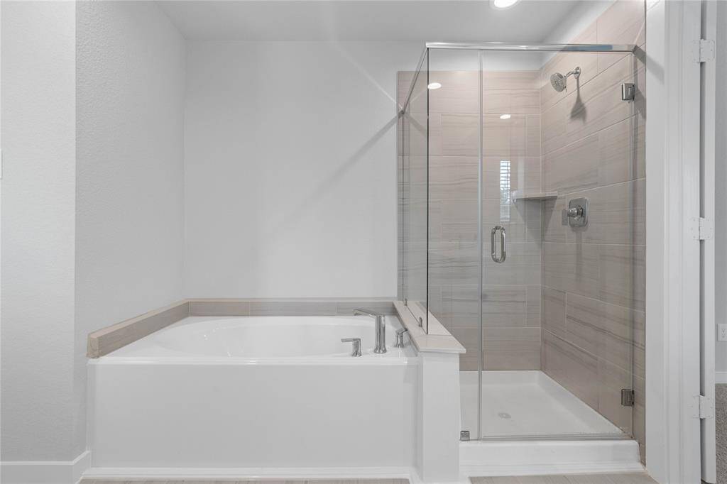 Additional view of the primary bathroom features dark framed walk-in shower with tile surround, and separate garden tub for soaking after a long day with custom tile detailing!
