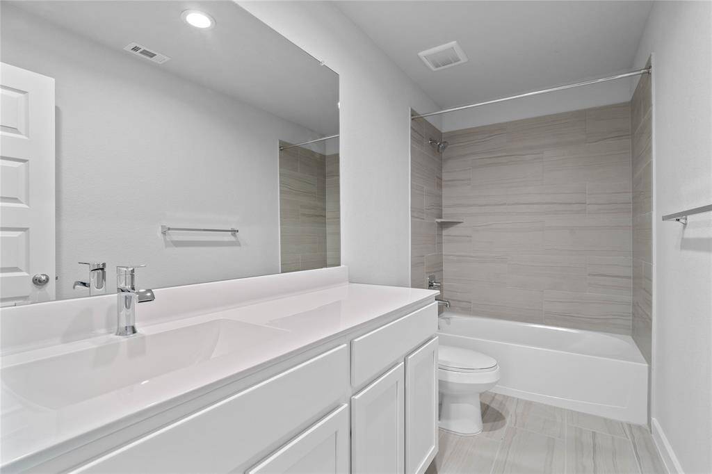 Secondary bath features tile flooring, bath/shower combo with tile surround, stained wood cabinets, beautiful light countertop, mirror, dark, sleek fixtures and modern finishes!